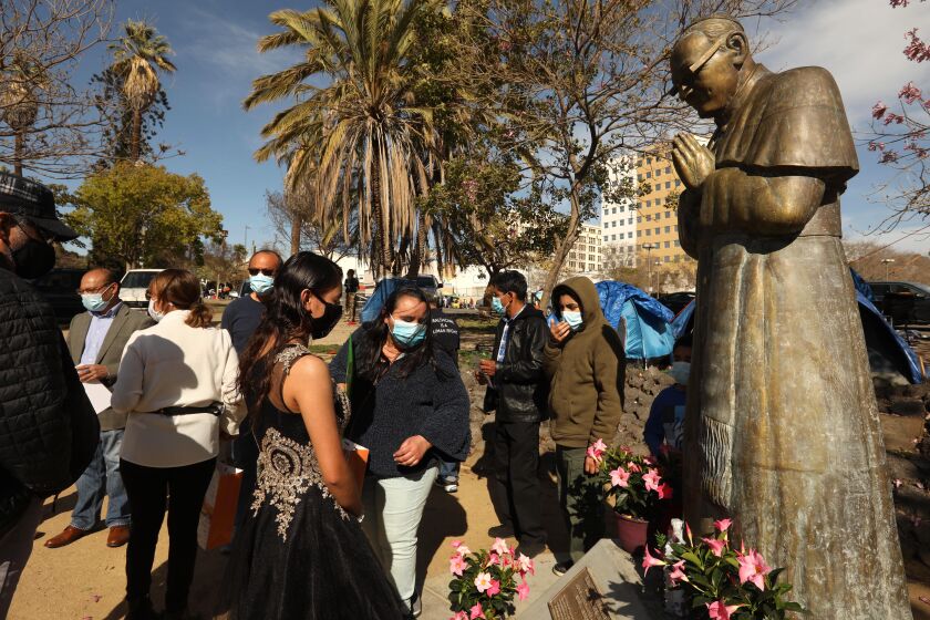 LOS ANGELES, CA - MARCH 24, 2021 - - A statue of Archbishop Oscar Romero seems to pray over members from the Salvadoran community in Los Angeles who gathered to remember Romero on the 41st anniversary of his death at San Romero Plaza in MacArthur Park on March 24, 2021. Archbishop Romero was shot to death by an assassin on March 24, 1980 while celebrating mass in the chapel of the Hospital of Divine Providence. Due to the coronavirus pandemic only a small group of people showed up to remember Archbishop Romero according to Manuel Olmos, with Coordinar San Romero. Archbishop Romero spoke out against poverty, social injustice, assassinations, and torture amid a growing conflict between the military government and left-wing insurgents that led to the Salvadoran Civil War. Pope Francis canonized Romero as a saint on October 14, 2018. Murals with his image can still be found on walls and buildings throughout Los Angeles. (Genaro Molina / Los Angeles Times)