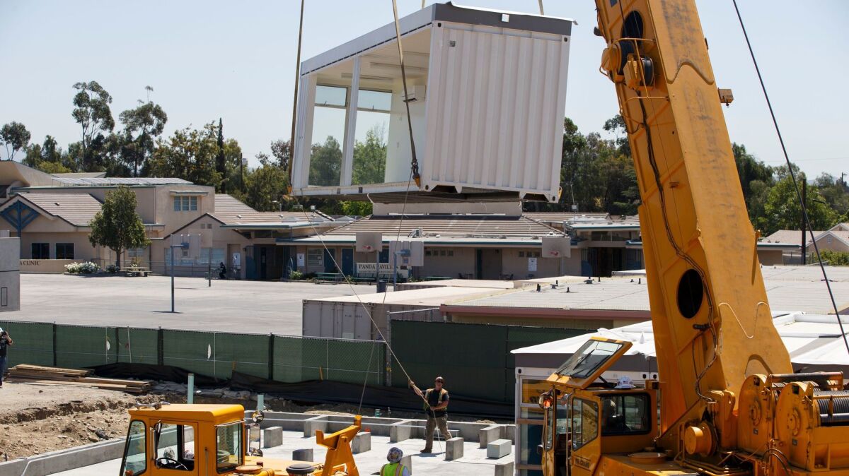 Construction workers use a crane to lift prefabricated classroom sections made of recycled shipping containers into position at Vaughn Next Century Learning Center.