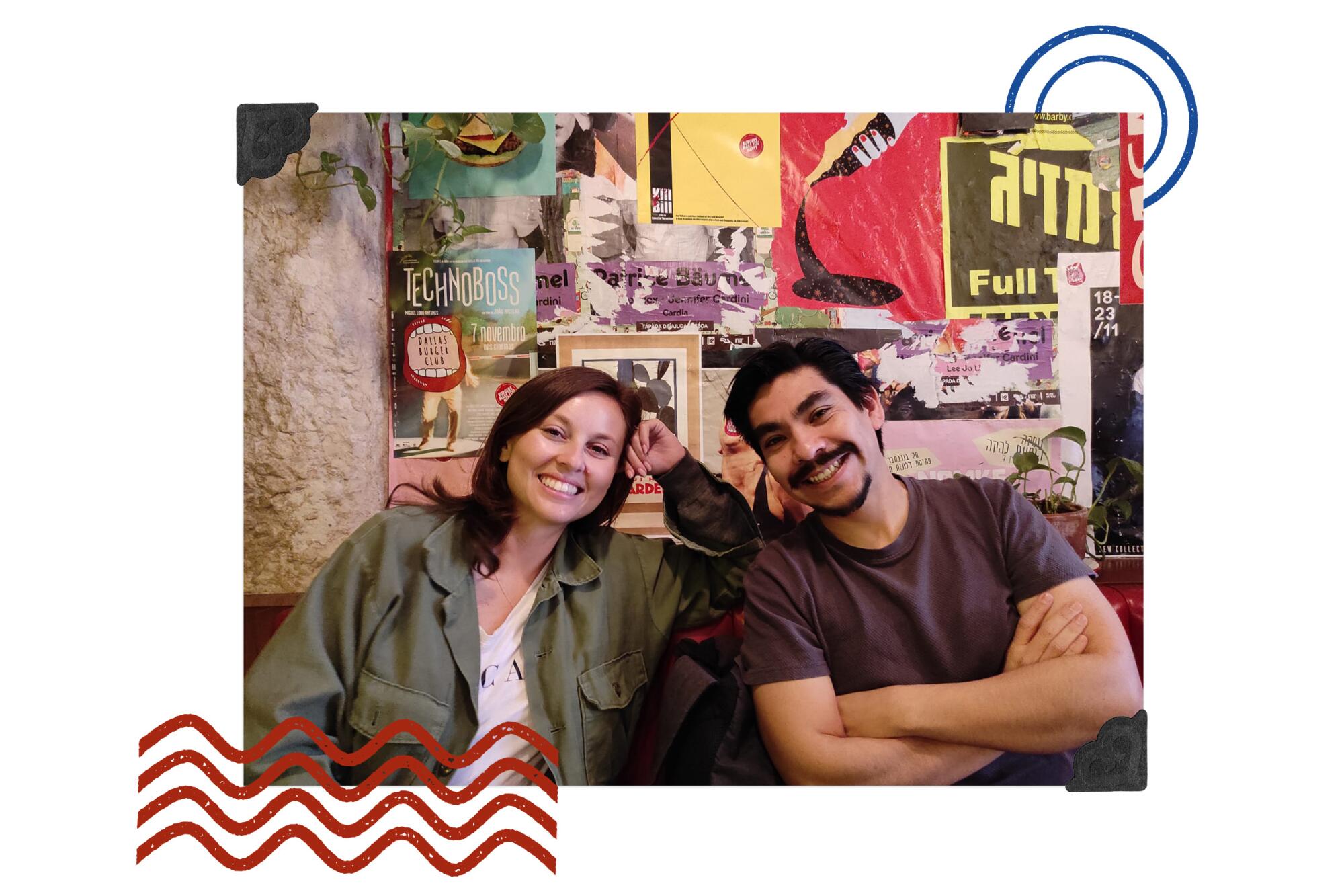 A smiling woman and man lean in for a photo in front of a wall of posters.