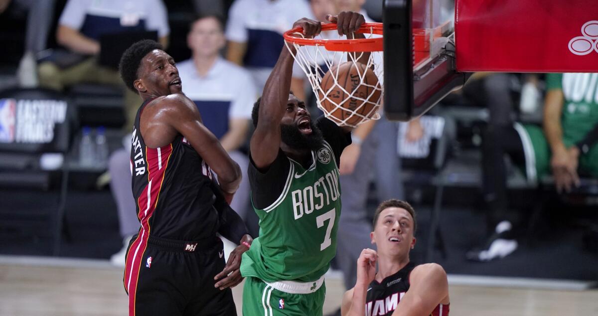 Boston Celtics guard Jaylen Brown (7) dunks the ball between Miami Heat's Bam Adebayo, left, and Duncan Robinson.