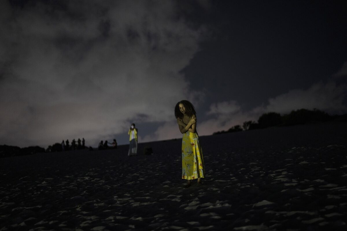 A woman prays in an area of the Abaete dune system, on a steep rise of sand evangelicals have come to call the "Holy Mountain", in Salvador, Brazil, late Friday night, Sept. 16, 2022. Evangelicals have been converging on the dunes for some 25 years but especially lately, with thousands now coming each week to sing, pray and enter trancelike states to commune with God.(AP Photo/Rodrigo Abd)