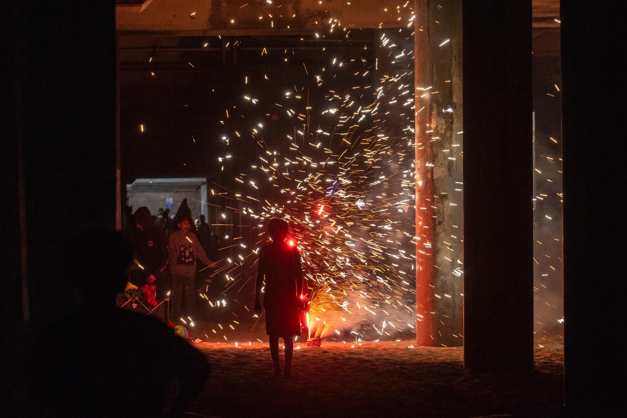 A person watches fireworks under the pier before the official fireworks show over the pier and ocean in Huntington Beach.