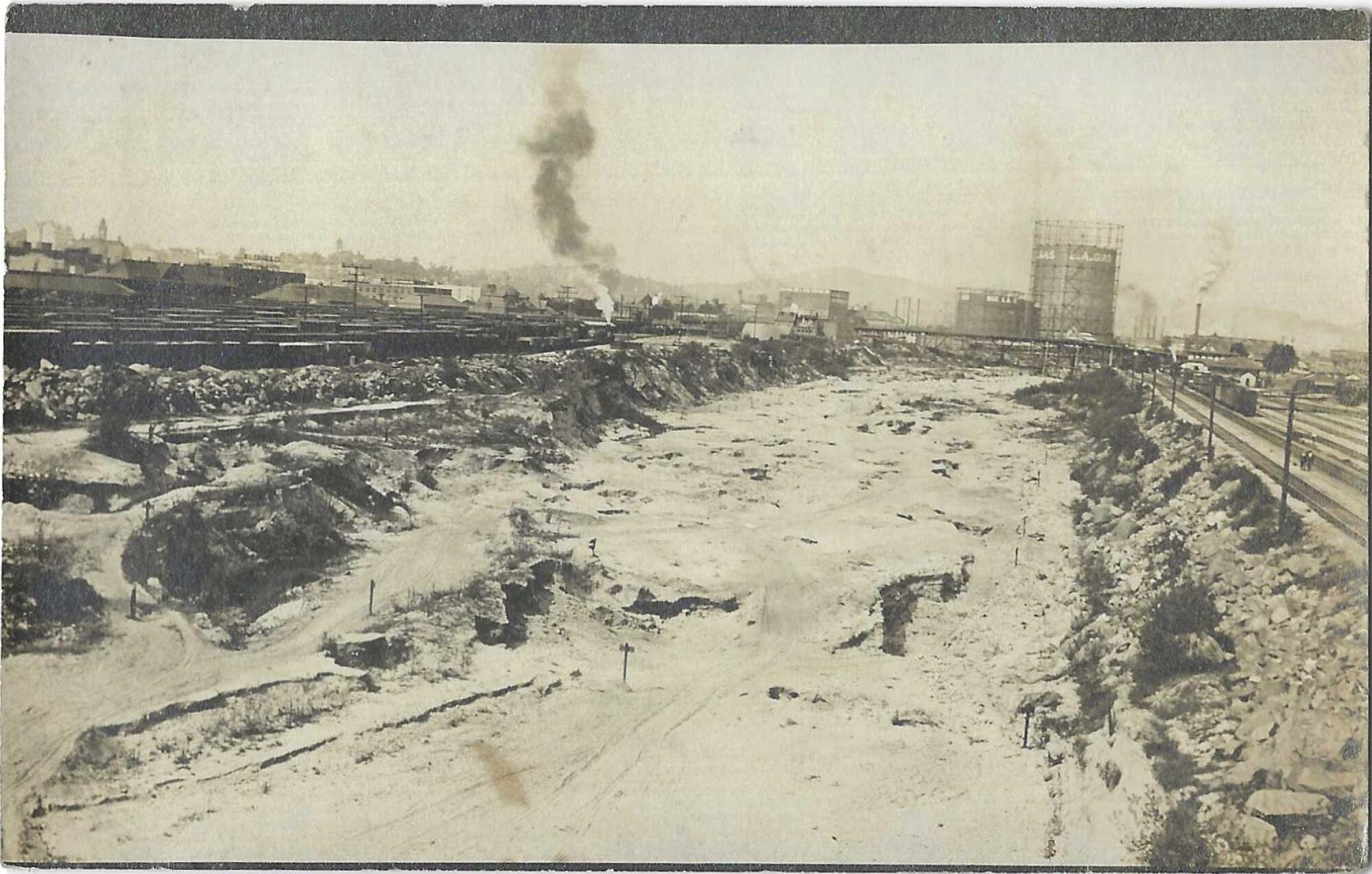 Black and white vintage postcard from Patt Morrison's collection, showing a dry L.A. River with rail and industry alongside.