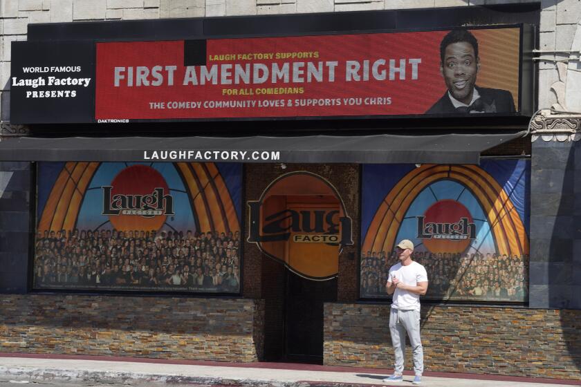 Un hombre parado bajo un mensaje de apoyo al comediante Chris Rock en la marquesina digital del club de comedia Laugh Factory, en Los Ángeles, el miércoles 30 de marzo de 2022. Rock fue abofeteado en el escenario por el ganador del Oscar al mejor actor, Will Smith, tras hacer un chiste sobre su esposa, Jada Pinkett Smith, durante la ceremonia del domingo. (Foto AP/Chris Pizzello)