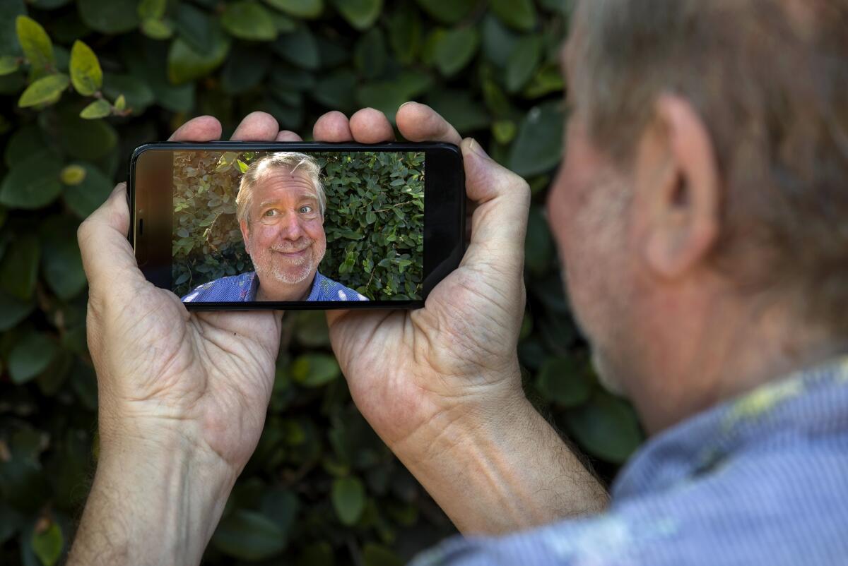 A man holds his phone in two hands while recording a selfie video of himself