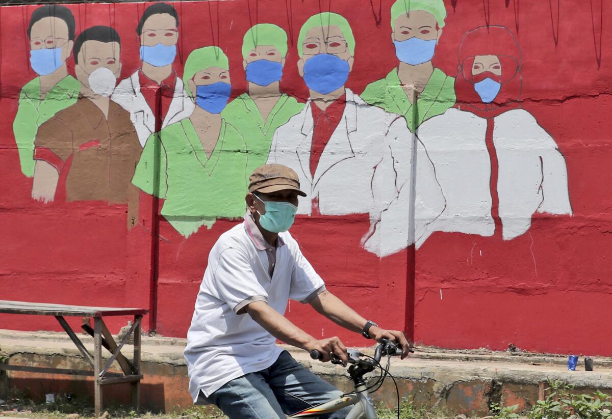 Una persona monta bicicleta frente a un mural sobre coronavirus en Yakarta, Indonesia.