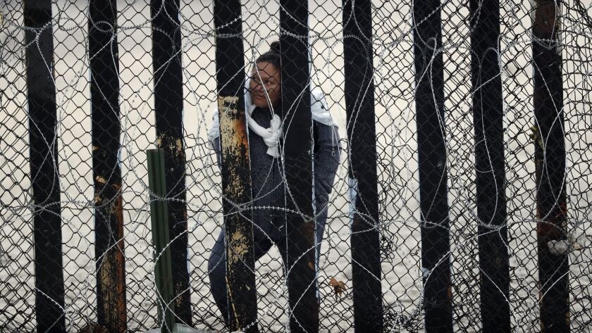 A woman in Tijuana looks through a section of the border wall.
