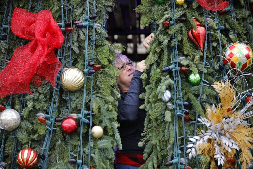 Volunteer Margaret Richardson of Del Cerro Baptist Church helps put the final touches on The Christmas Story Tree in the rain, which has been a tradition for more than 35 years at the Organ Pavilion during December Nights.