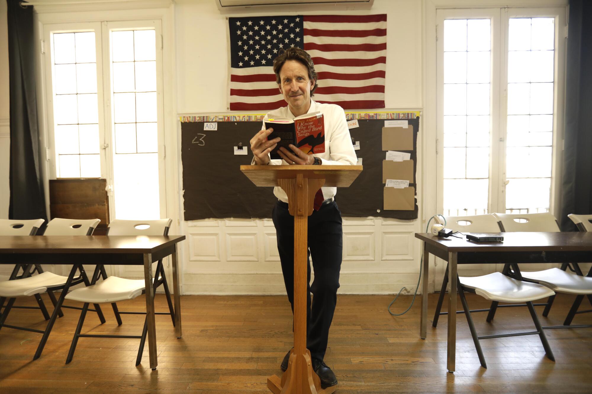 A man holds a book in front of an empty classroom.