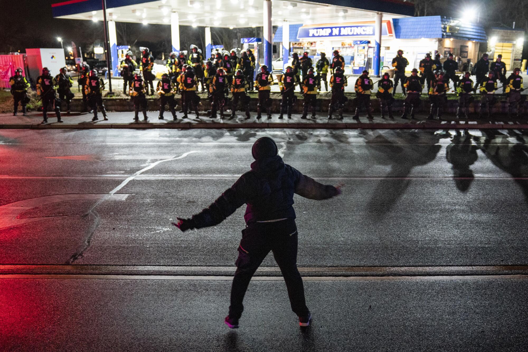 A protester is silhouetted against a line of police in front of a gas station