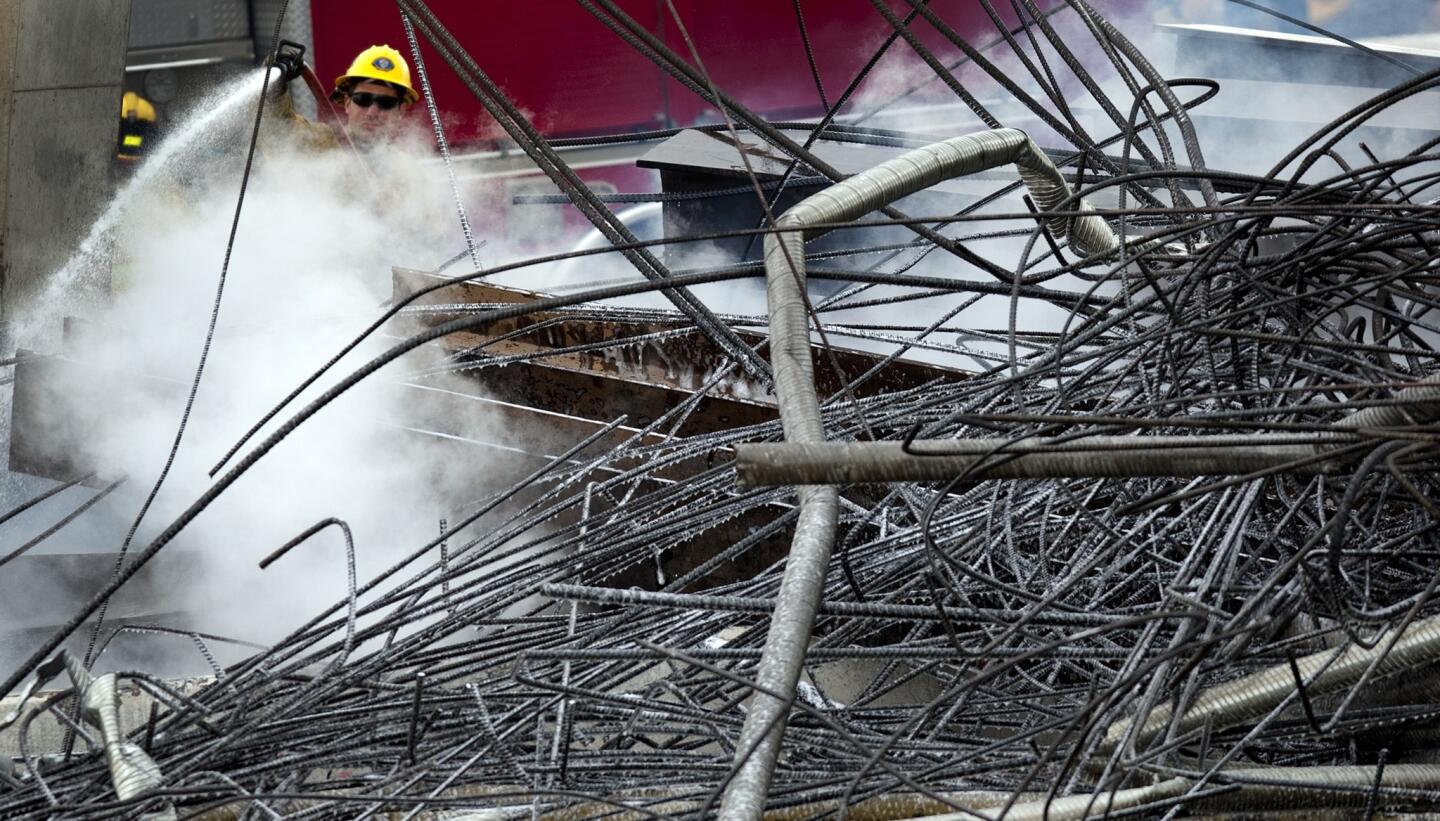 A San Bernardino County firefighter douses hot spots in the twisted metal and rebar remains of the Ranchero Road overpass on Interstate 15 in Hesperia.