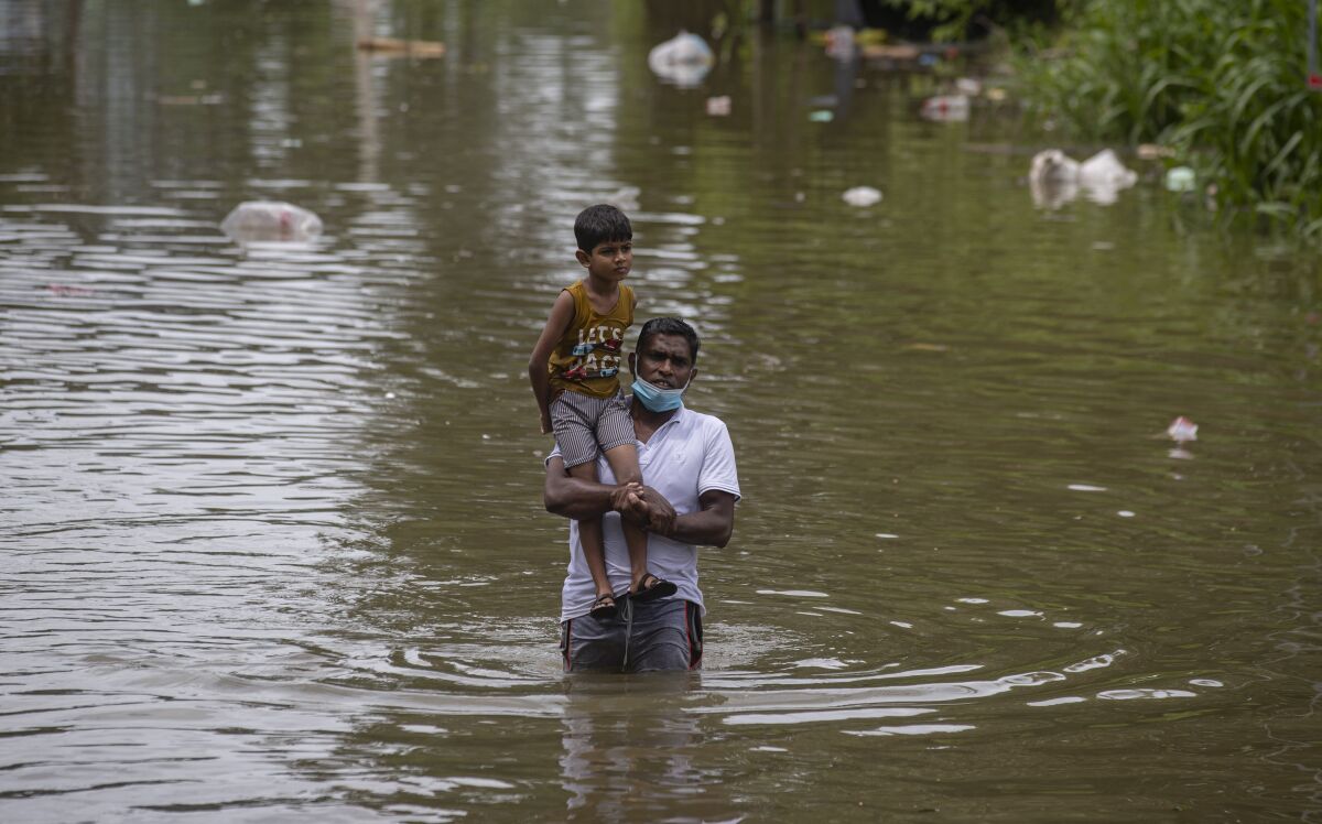 A Sri Lankan man wades through in an inundated street carrying a child following heavy rainfall at Malwana, on the outskirts of Colombo, Sri Lanka, Saturday, June 5, 2021. Flash floods and mudslides triggered by heavy rains in Sri Lanka have killed at least four people and left seven missing, while more than 5,000 are displaced, officials said Saturday. Rains have been pounding six districts of the Indian Ocean island nation since Thursday night, and many houses, paddy fields and roads have been inundated, blocking traffic. (AP Photo/Eranga Jayawardena)