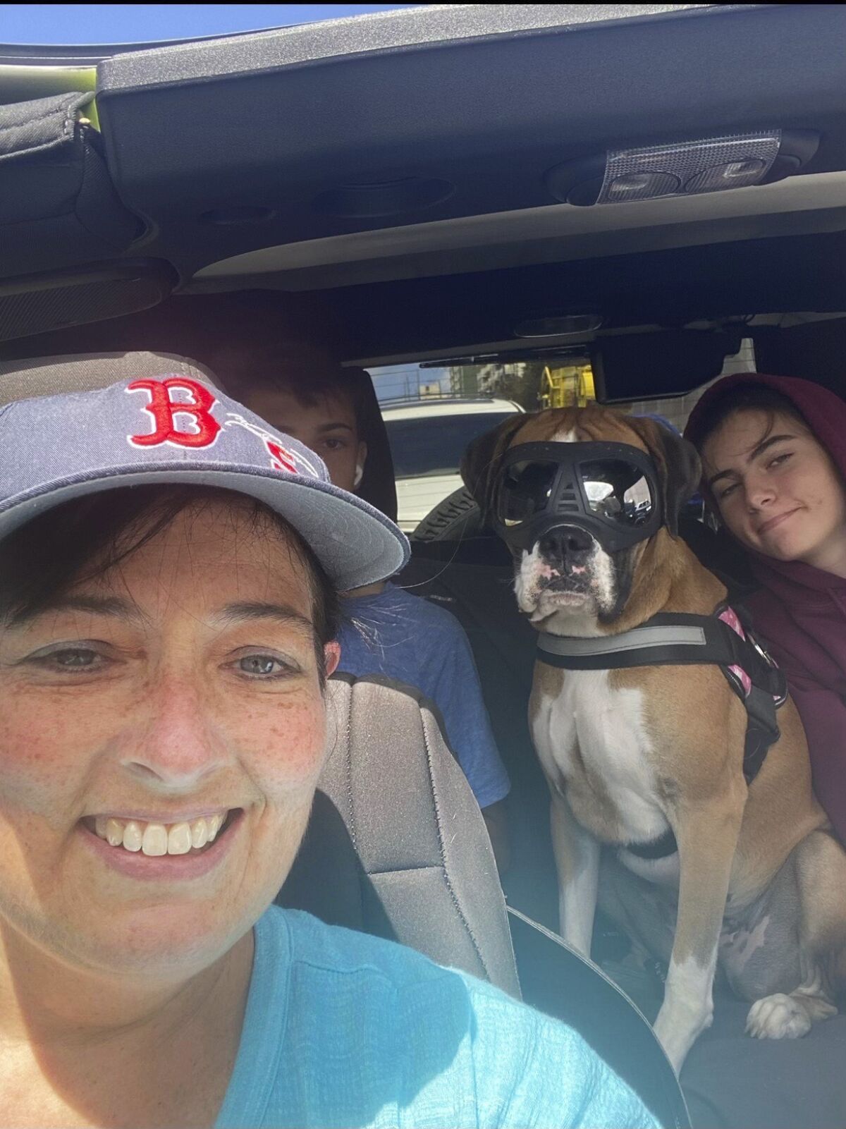 Selfie of a woman, her children and their dog, wearing goggles, in a car