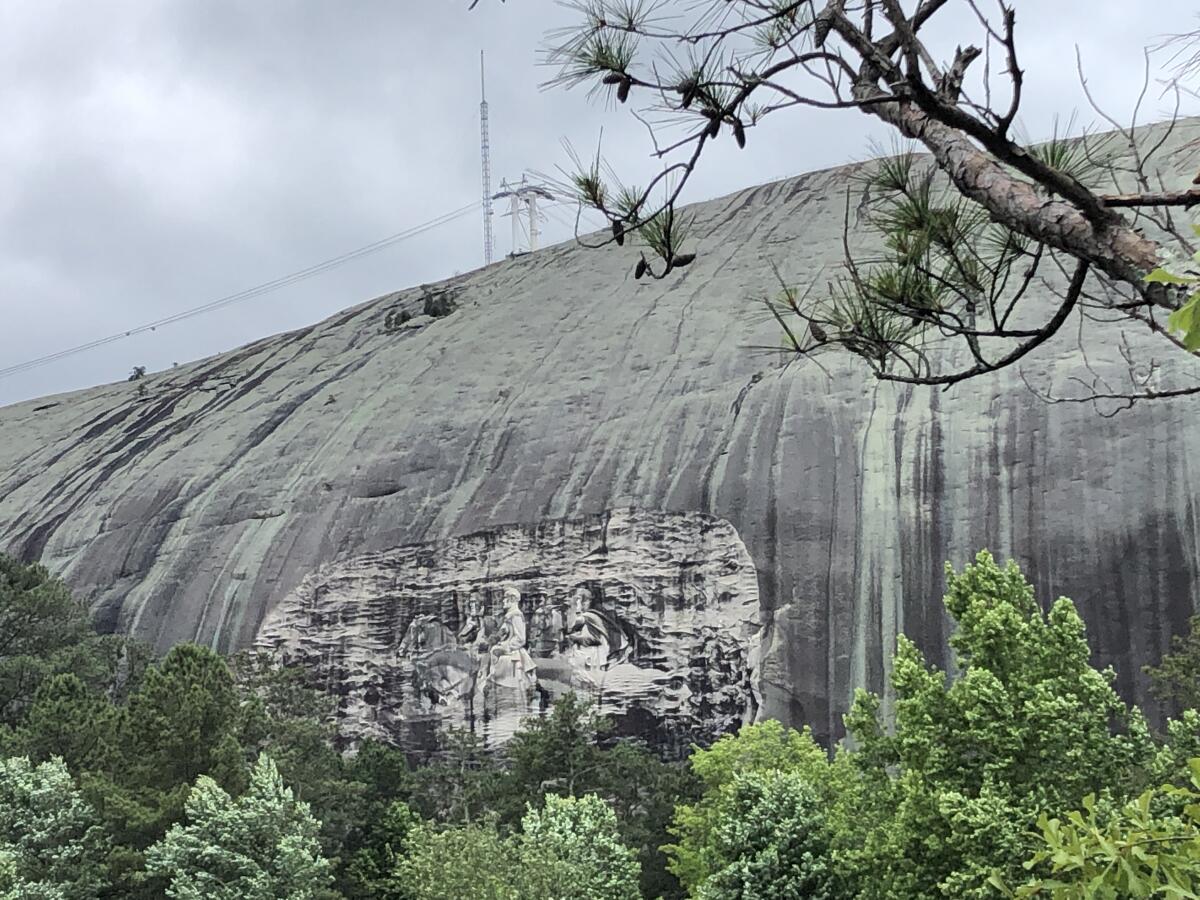 A bas relief of Confederate leaders on horseback is carved into a massive granite outcropping seen between tree branches.