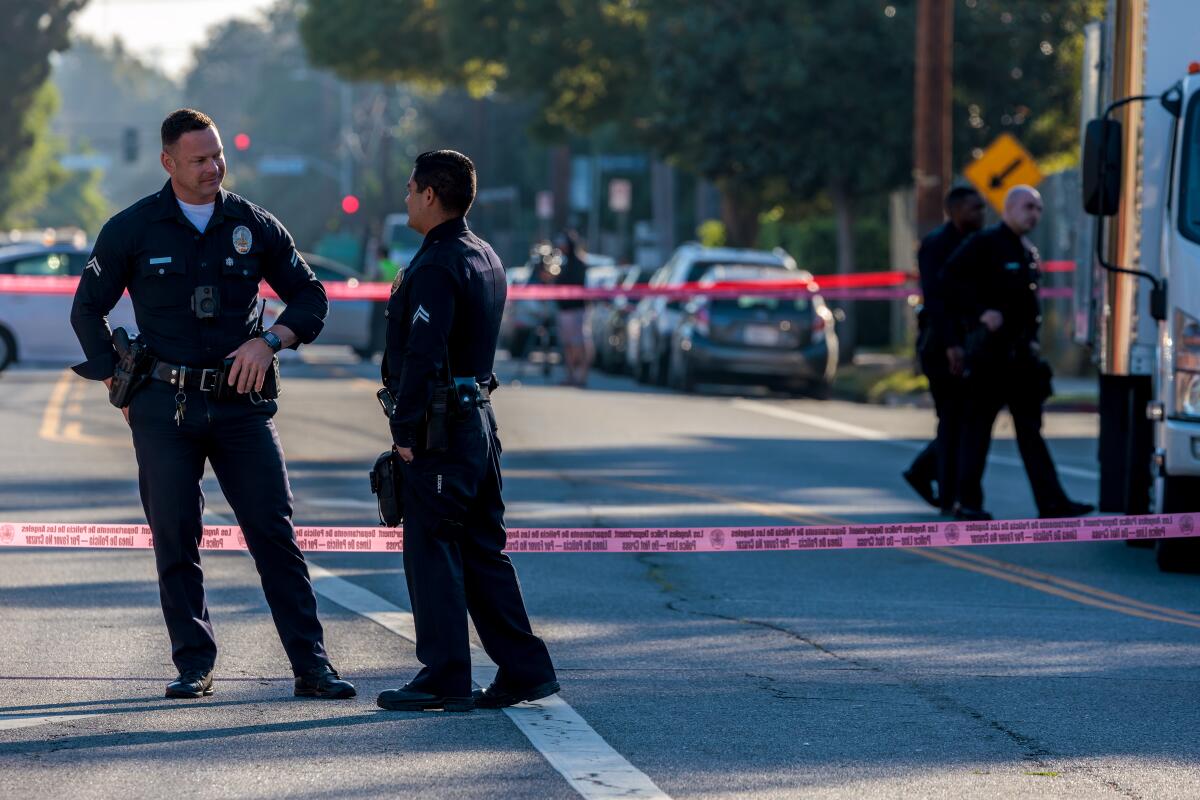 Two police officers talk while standing in the street behind crime scene tape