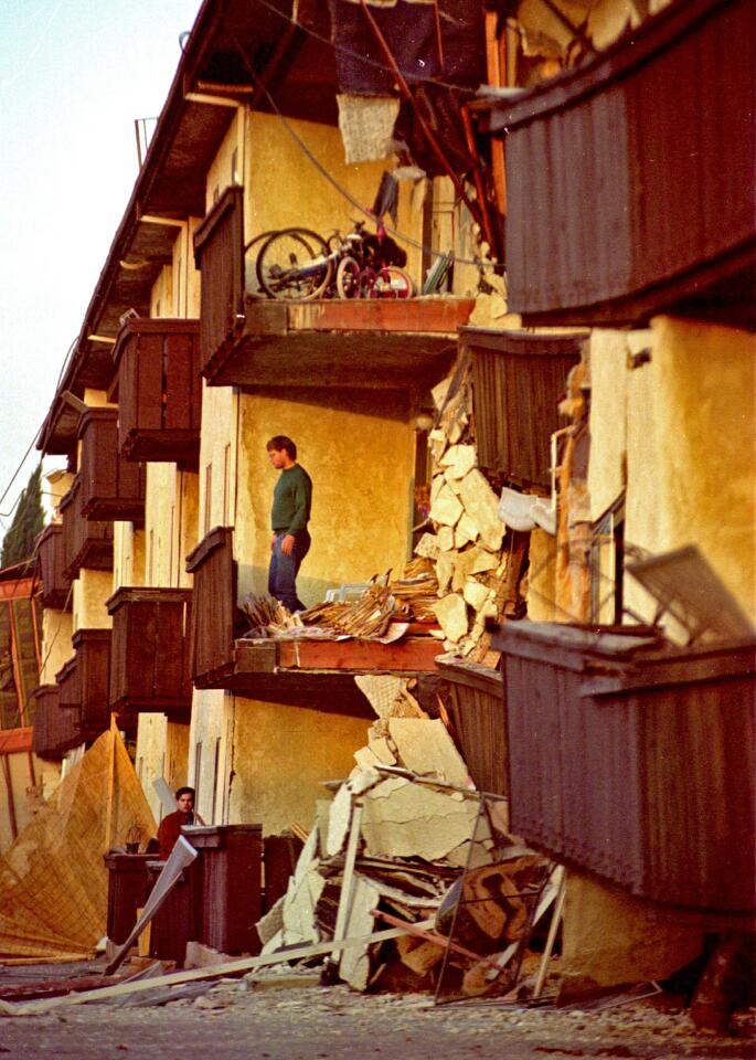 A man stares out to the street from his wall-less home at the devastated Northridge Meadows apartments.