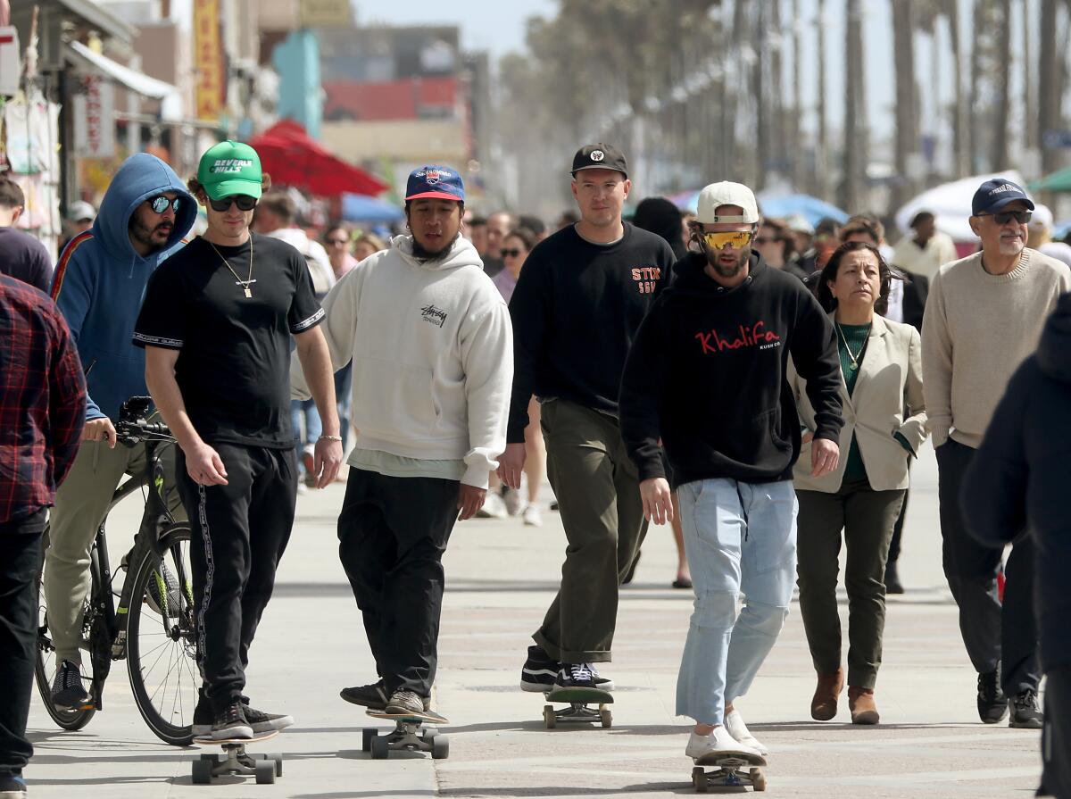 Four men on skateboards in the middle of a crowded sidewalk