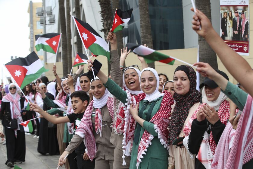Jordanos ondean banderas previo a que pase la caravana del príncipe heredero Hassan y su esposa Rajwa Alseif, durante las celebraciones por su boda, en Amán, el jueves 1 de junio de 2023. (AP Foto/Raad Adayleh)