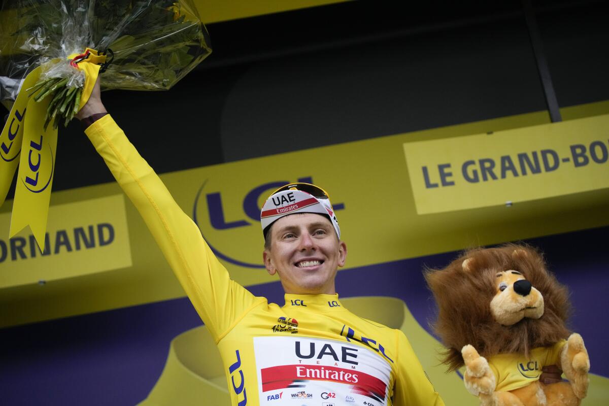 Tadej Pogacar, wearing the overall leader's yellow jersey, raises his arm