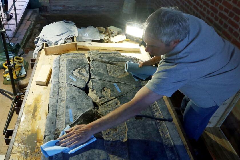 In this Tuesday, May 9, 2017 photo, monument Conservator Jonathan Appell, right, works to clean a 6-foot black stone slab which was rediscovered in the 1617 church at historic Jamestown, Va. Six months after launching a painstaking probe aimed at English America's second oldest church, Jamestown archaeologists have unearthed a jumbled historical puzzle that reaches back 400 years. (Aileen Devlin/The Daily Press via AP)
