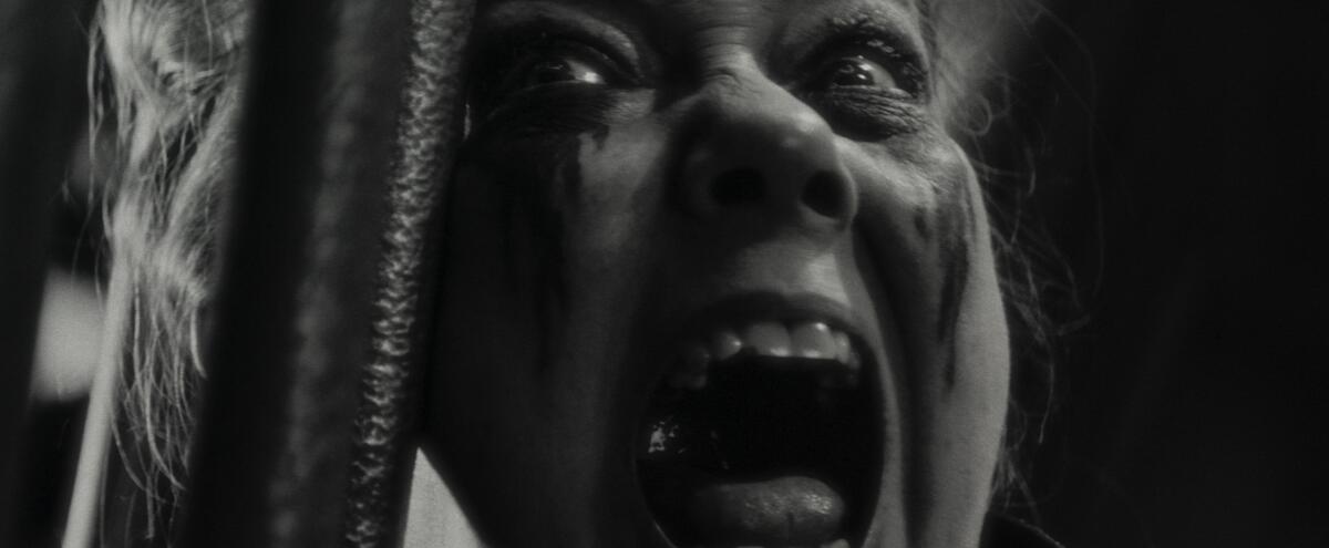 Close-up of a woman with mascara running down her face, pressed against bars as she screams.