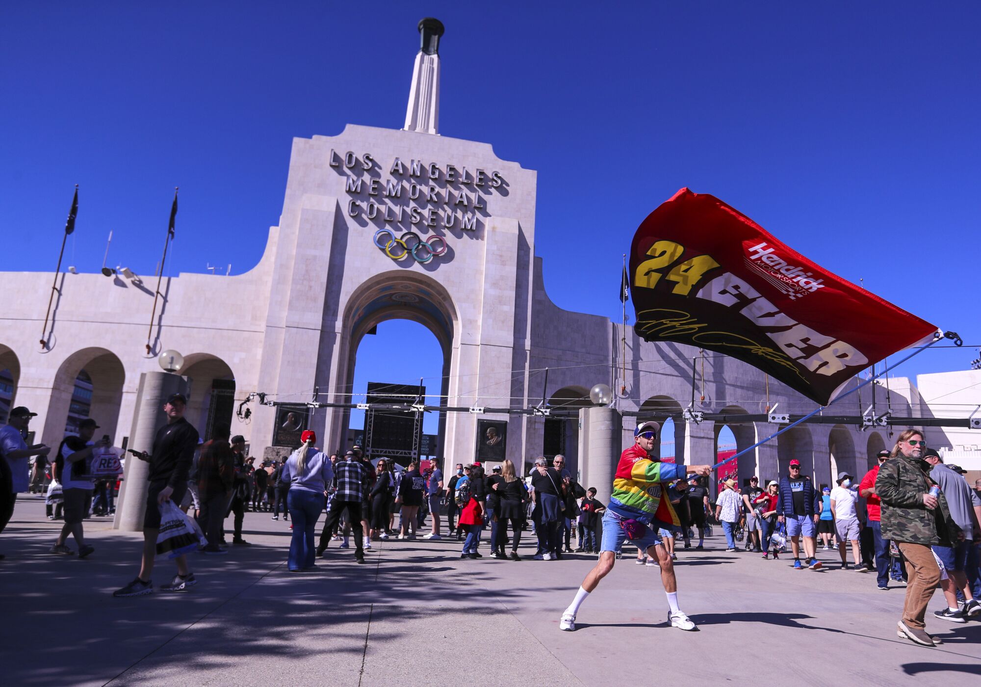 Corvette Racing driver Jordan Taylor waves a racing flag as fans arrive at the Coliseum.