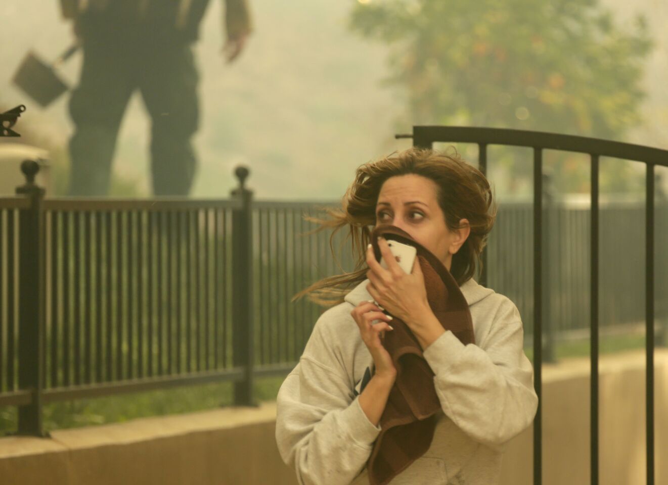 Rita Abouchedid covers her face from heavy smoke as fire approaches her home on Kregmont Drive in Glendora.