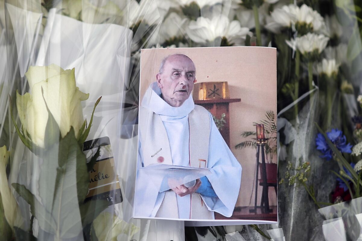 FILE - A picture of late Father Jacques Hamel is placed on flowers at the makeshift memorial in front of the city hall closed to the church where an hostage taking left a priest dead the day before in Saint-Etienne-du-Rouvray, Normandy, France, Wednesday, July 27, 2016. Four people go on trial on Monday Feb.14, 2022 on charges of terrorist conspiracy after the murder of a Catholic priest in a Normandy church in 2016. Father Jacques Hamel was killed by two 19-year-old attackers as he celebrated Mass on a quiet summer weekday in the small Normandy town of Saint-Etienne-du-Rouvray. (AP Photo/Francois Mori, File)