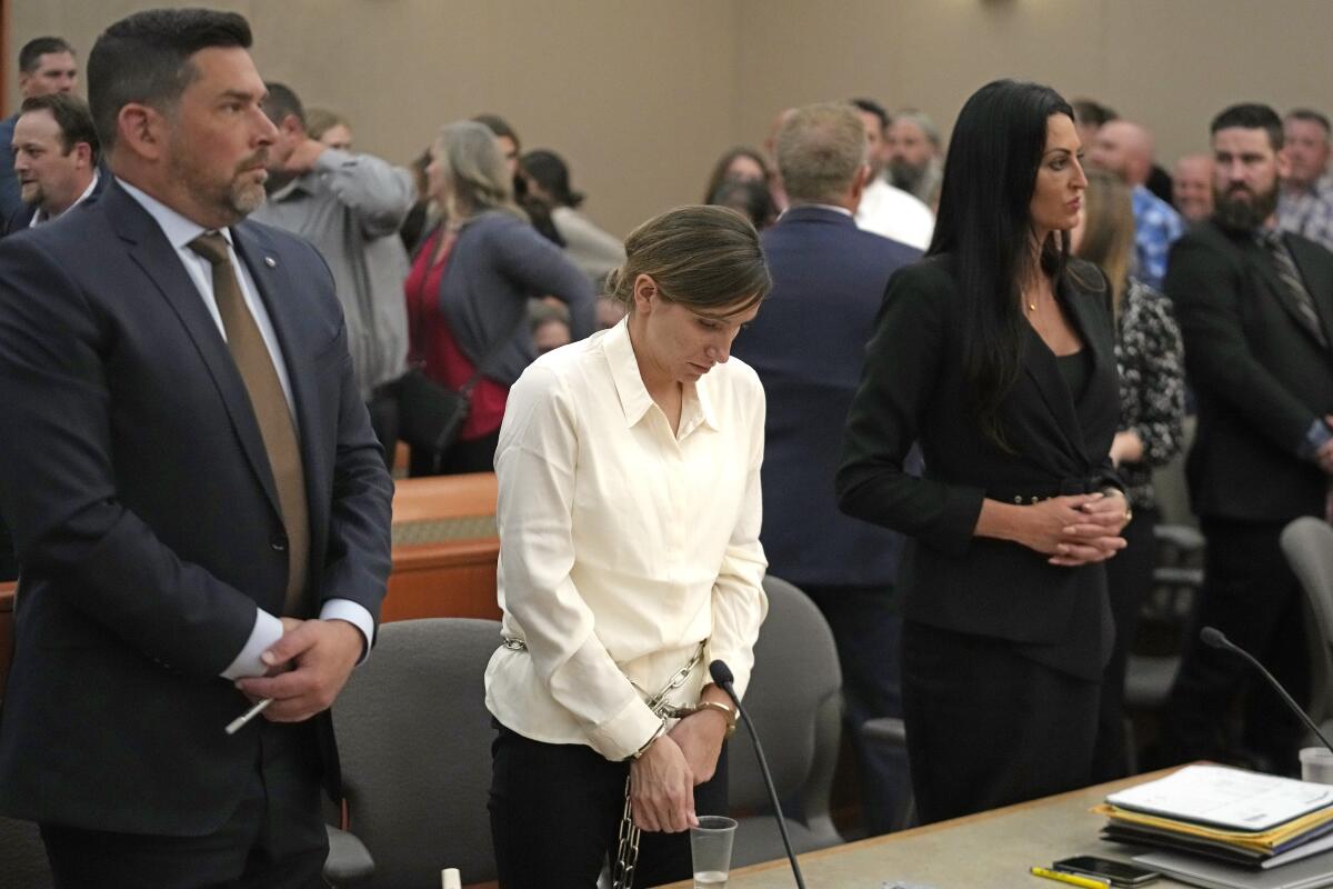 A woman in handcuffs stands with her head lowered in court. 