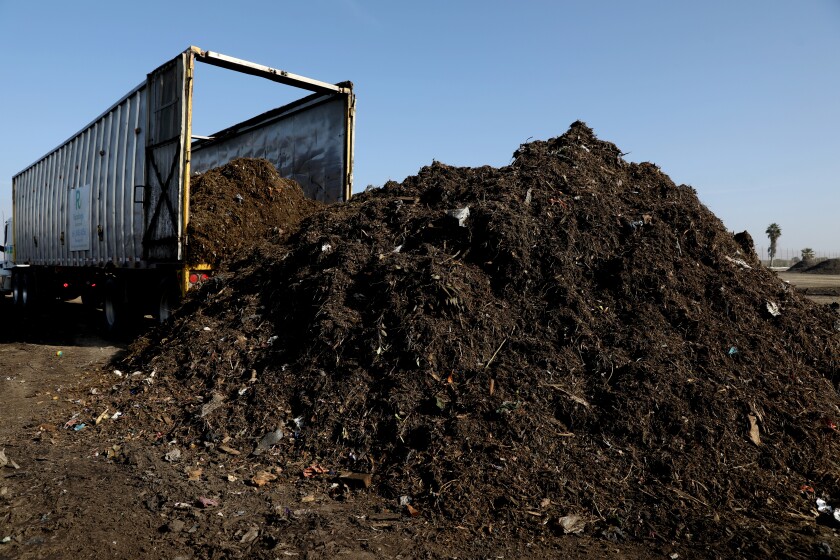 A tractor-trailer unloads raw materials that will be turned into compost.
