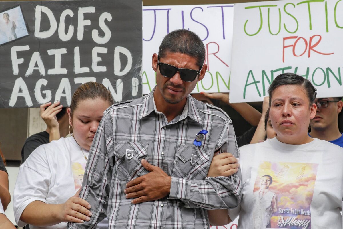 A man supported by 2 women. Posters are behind them, one reading "DCFS failed again."