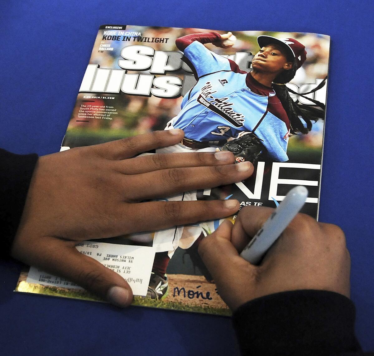 One hand holds down and another hand holds a Sharpie to sign a Sports Illustrated magazine 