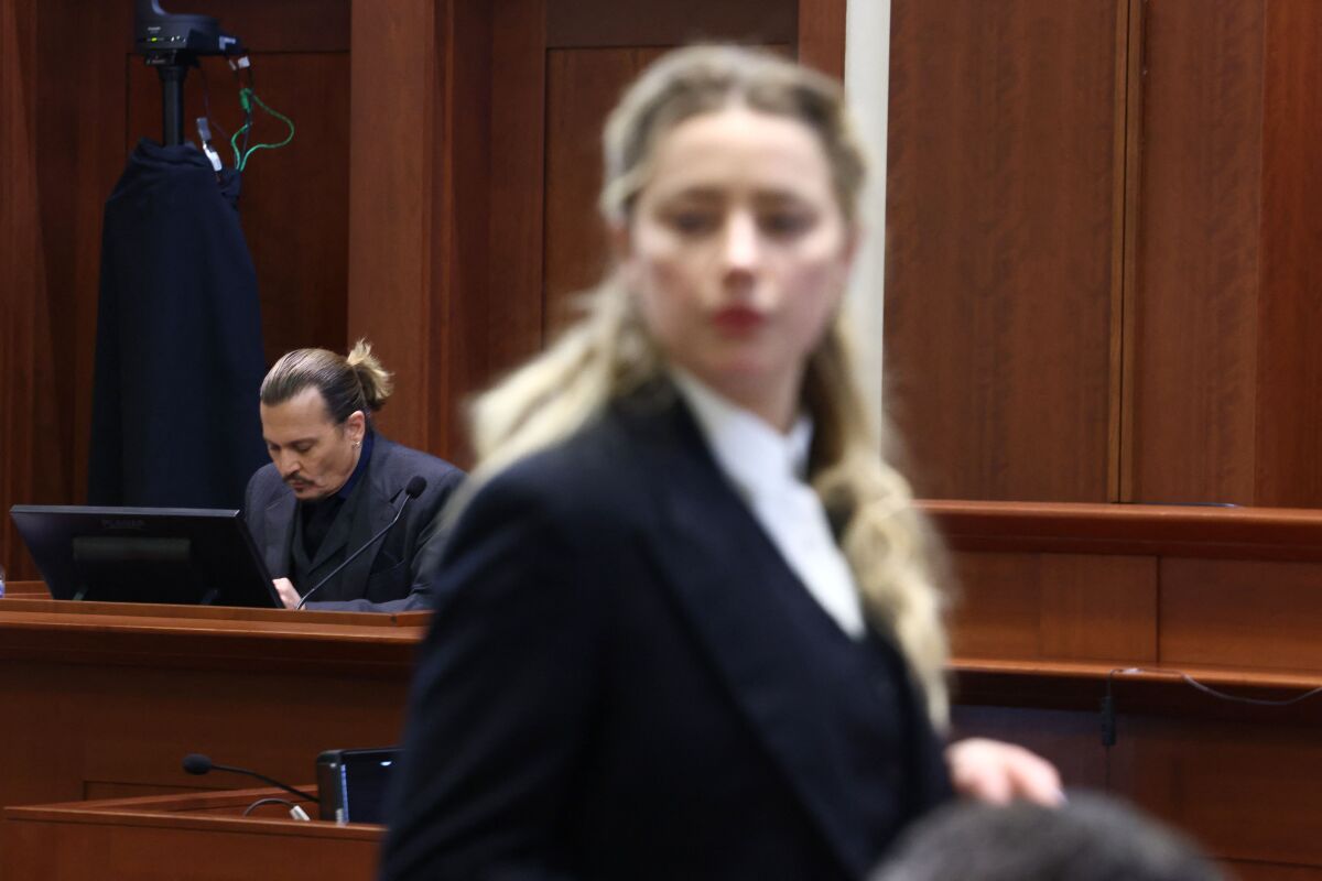 Johnny Depp on the witness stand with Amber Heard in the foreground.