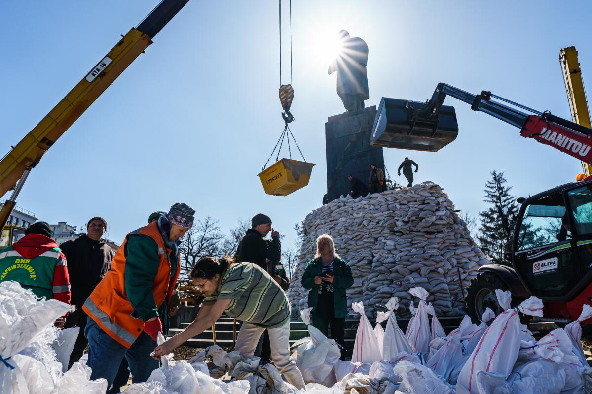 People load sandbags and pile them around an elevated statue