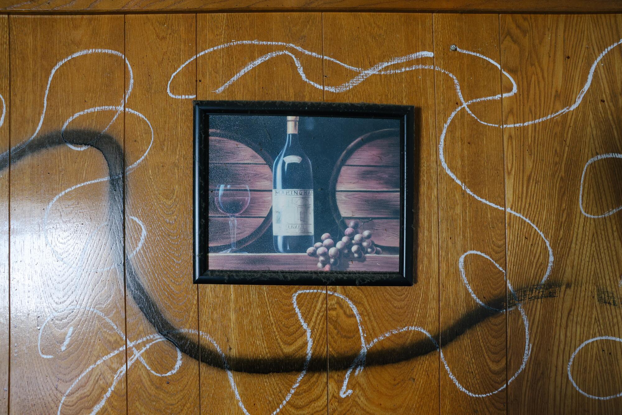 White swirls and a curved black line drawn on a wood-paneled wall next to framed art of a wine bottle, barrels and grapes
