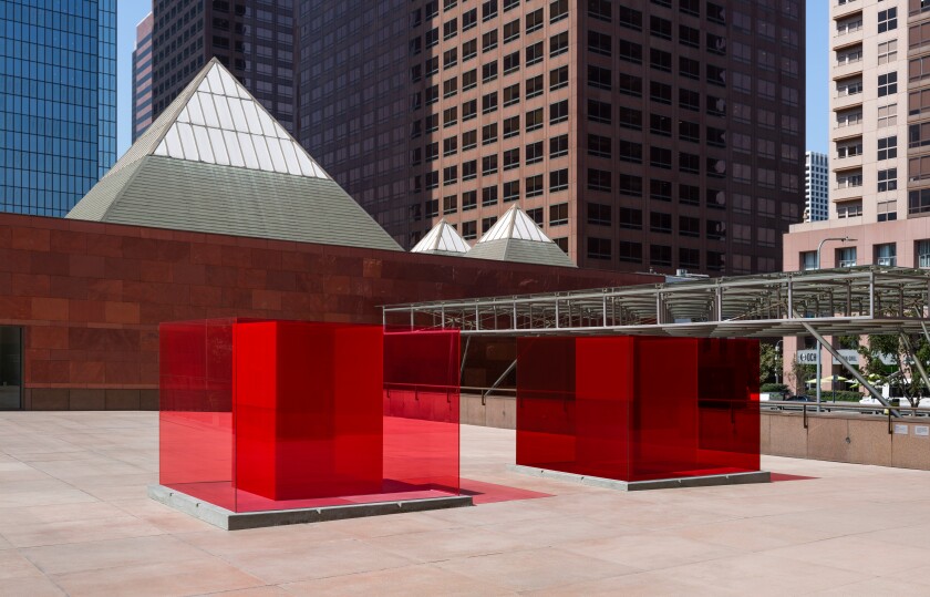 Two red glass boxes inside red glass boxes sit in a plaza surrounded by tall buildings