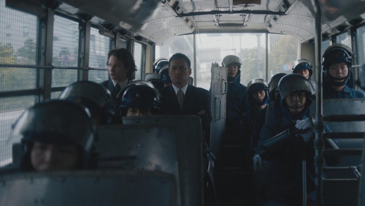A reporter and a detective ride in a bus with a bunch of policemen in heavy armor