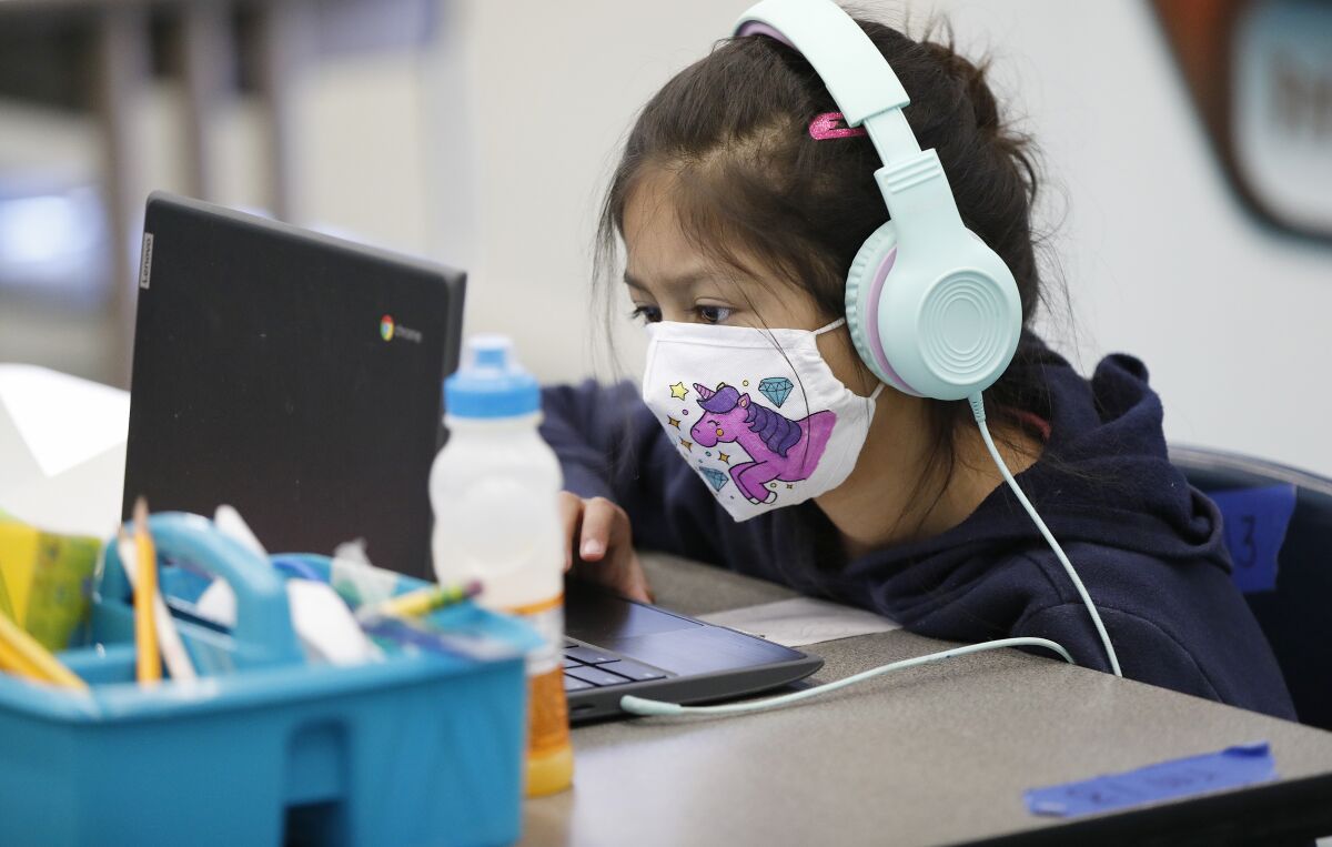 A child wears a mask and headphones and looks at a laptop.