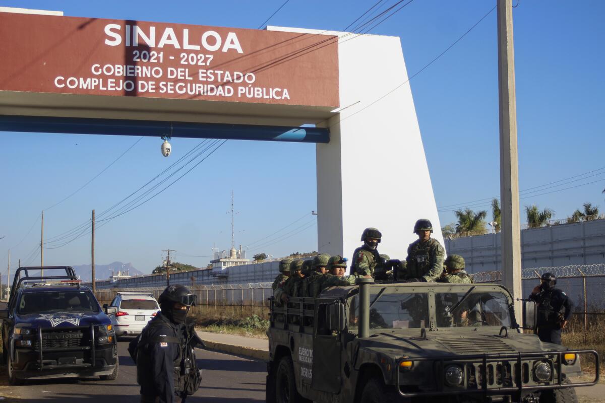 Police and military in vehicles and on foot pass under an arch identifying the Mexican state of Sinaloa. 