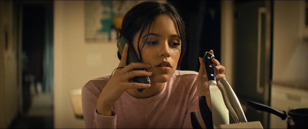 A woman talking on the phone while fiddling with a kitchen knife set 