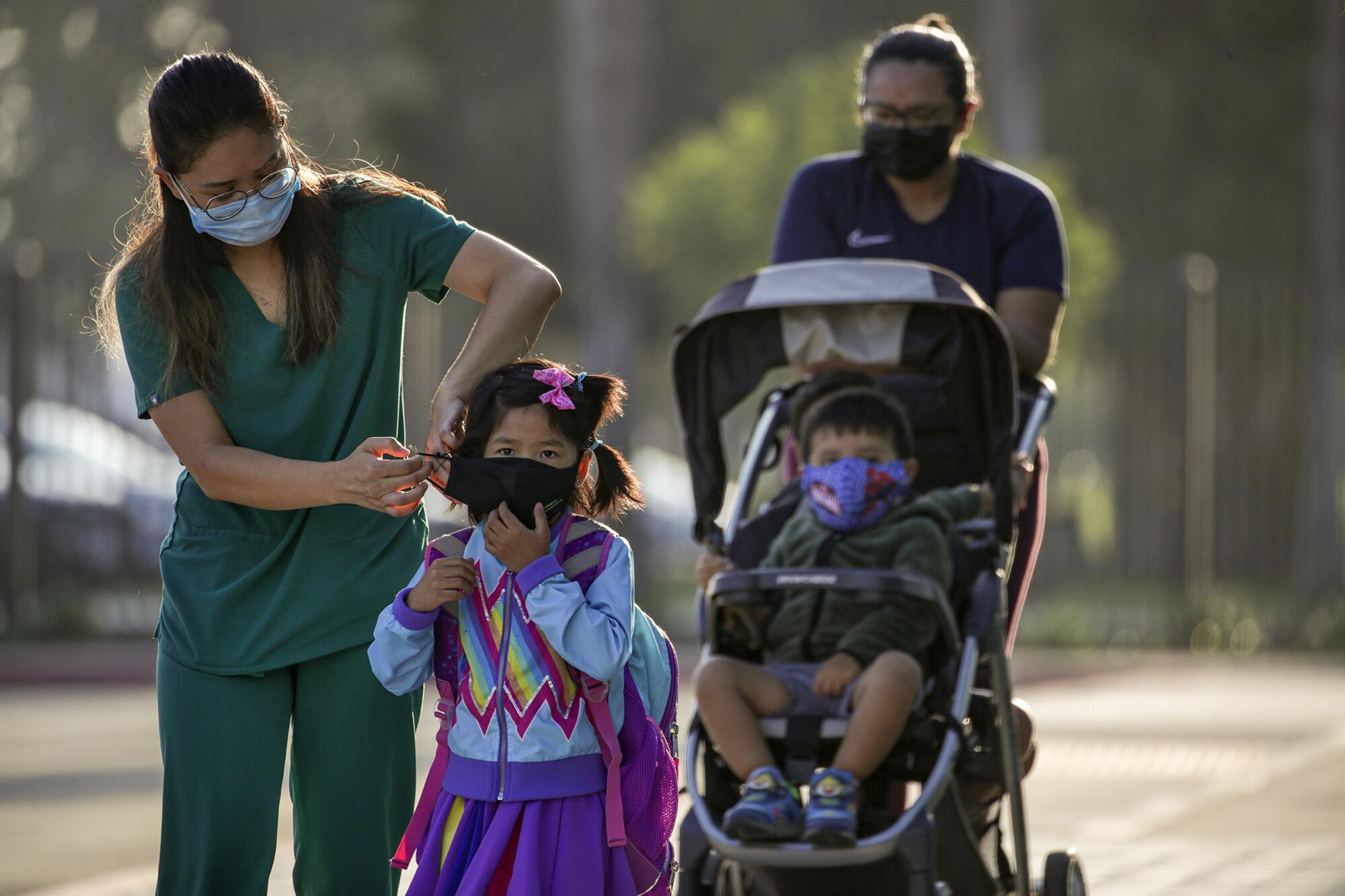 Uyen Nguyen, left, places a mask on her 6-year-old daughter, Mia, as they arrive at Theodore Roosevelt Elementary School.