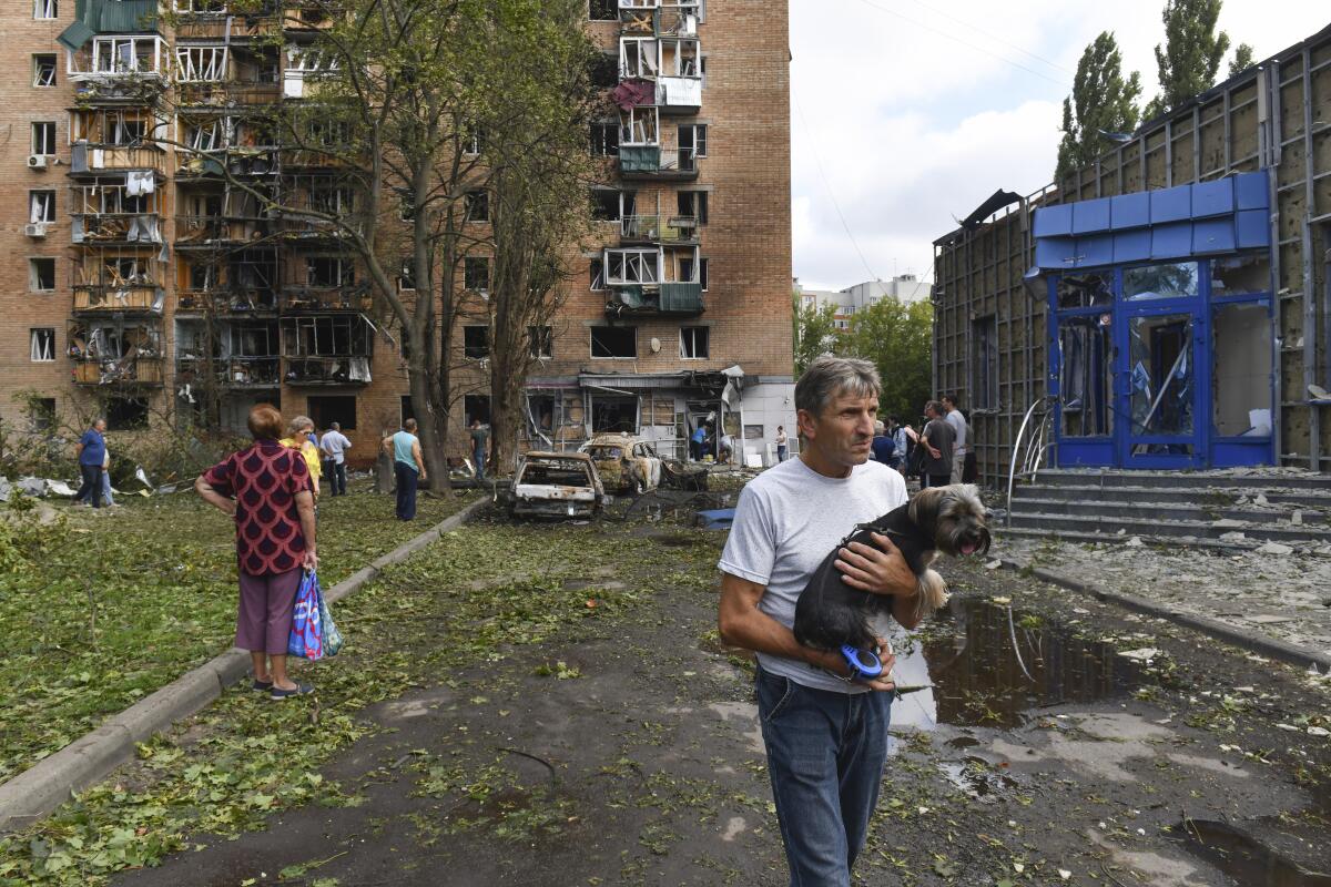 A man carries a dog outside a damaged building.