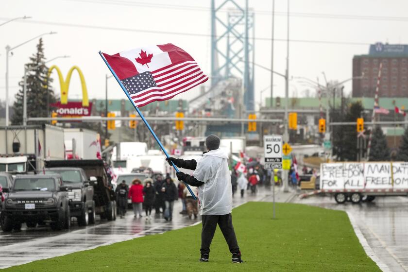 A man waves a Canadian and American flag as truckers and supporters block the access leading from the Ambassador Bridge, linking Detroit and Windsor, as truckers and their supporters continue to protest against COVID-19 vaccine mandates and restrictions, in Windsor, Ontario, Friday, Feb. 11, 2022. (Nathan Denette/The Canadian Press via AP)