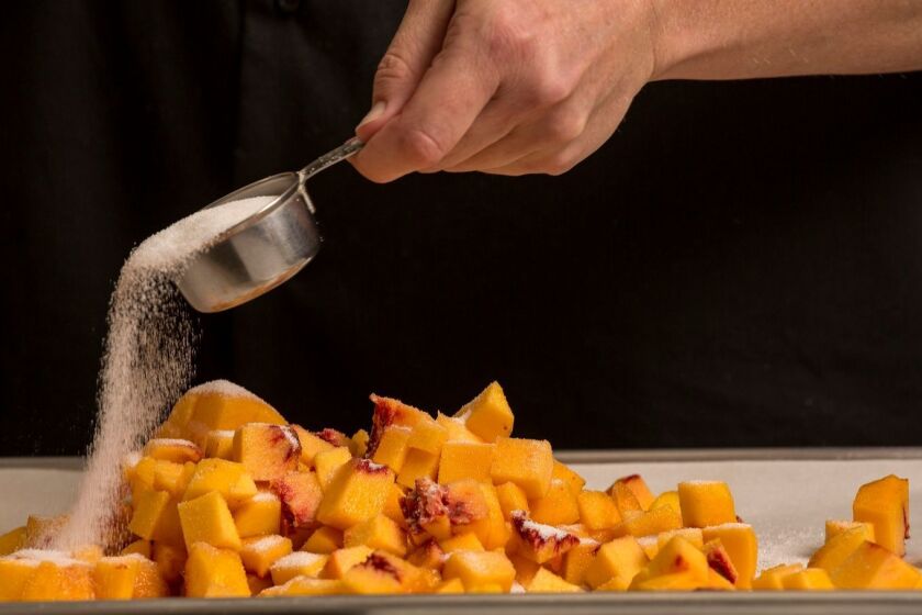 Diced peaches are coated with sugar for a frozen yogurt recipe being tried out in the Los Angeles Times test kitchen in 2016.