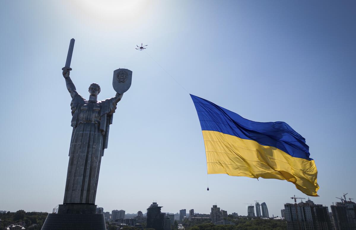 Drone towing large Ukrainian national flag next to large statue