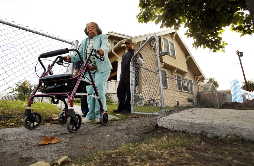 Geneva James, 84, who has lived in her home on the corner of St. Andrews Place and 48th Street since 1970 is helped by her nephew Maurice Stepter, right, as she tries to navigate over a distorted sidewalk in front of her home.