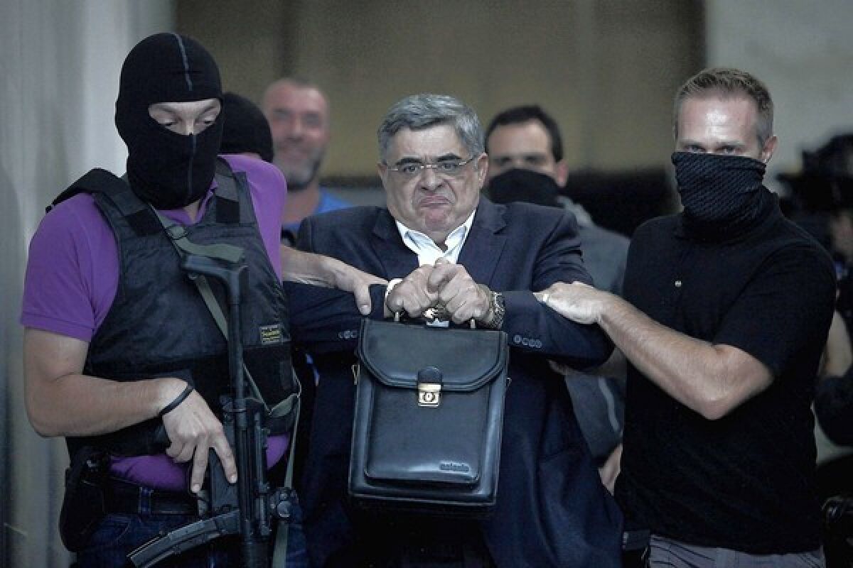 Nikos Michaloliakos, leader of Greece's far-right Golden Dawn party, is escorted by masked police officers Saturday to the prosecutor from police headquarters in Athens.