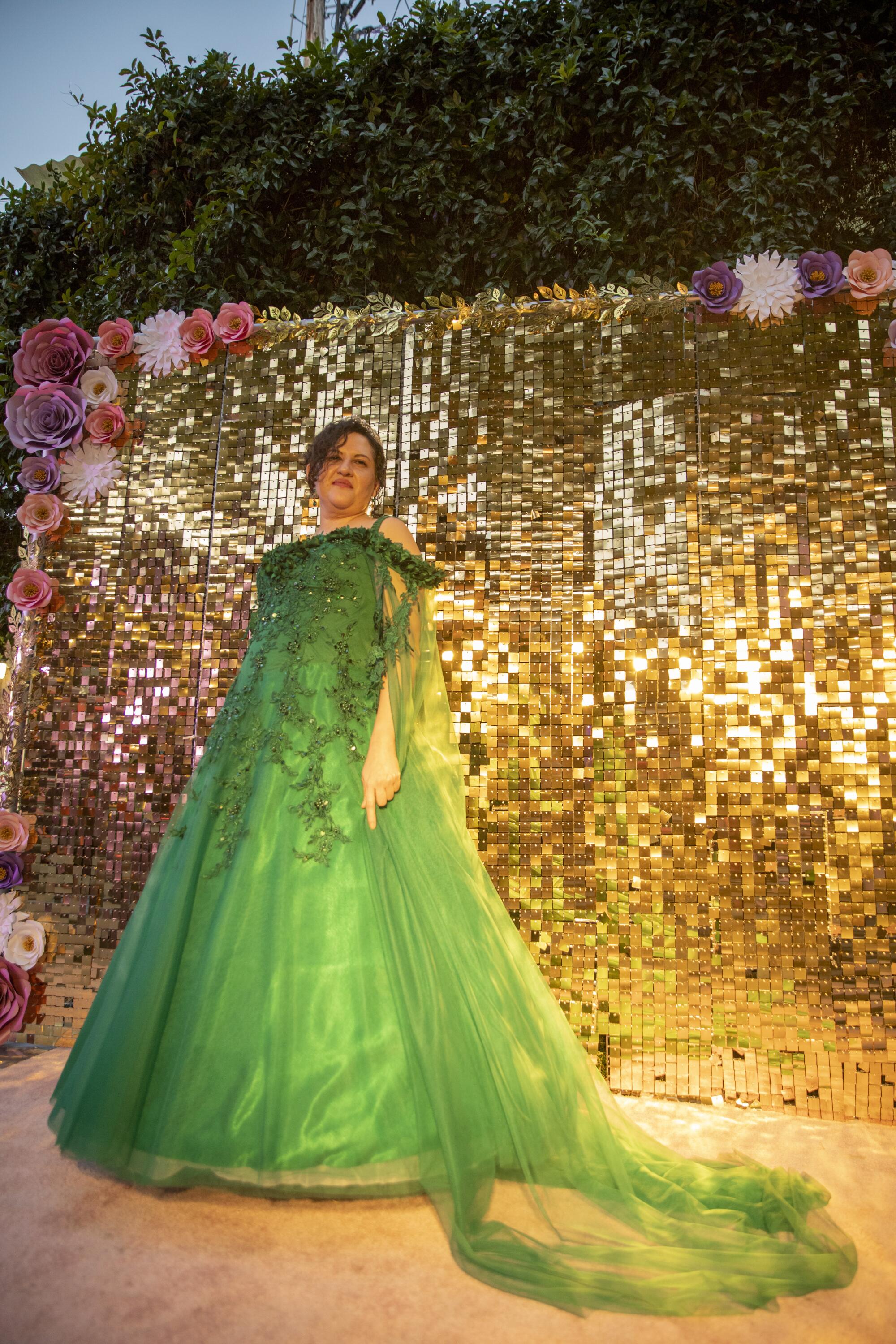 Cruz poses for a photo wearing a green dress in front of a glitter backdrop
