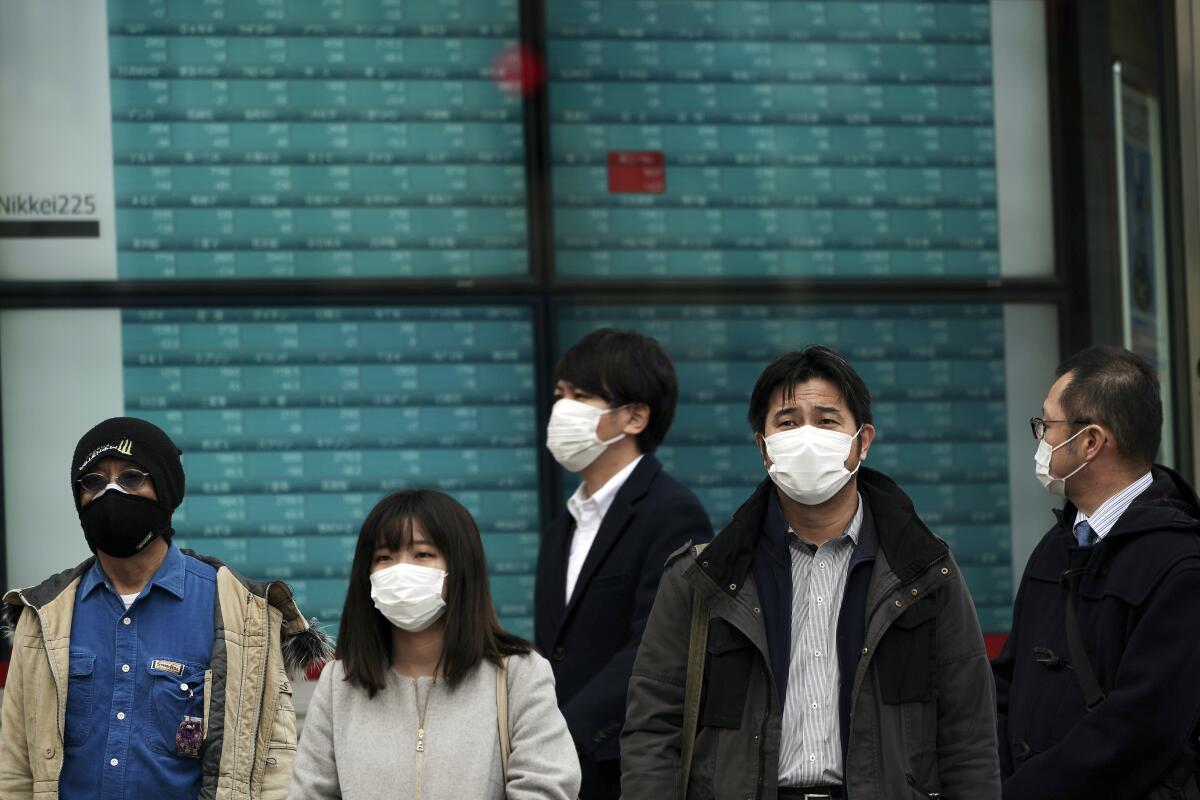 People wearing masks stand by an electronic stock board at a securities firm in Tokyo