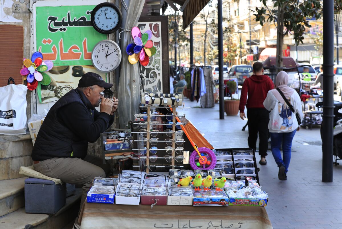 Salah Nasab, a Lebanese street vendor who also sells and repairs clocks, sits next of two clocks that show different times in Lebanon, in the southern port city of Sidon, Lebanon, March 27, 2023. Lebanon's caretaker prime minister reversed an unpopular decision made by his office to delay the start of daylight saving time by a month, saying Monday the Cabinet decided to implement the change in two days. (AP Photo/Mohammed Zaatari)